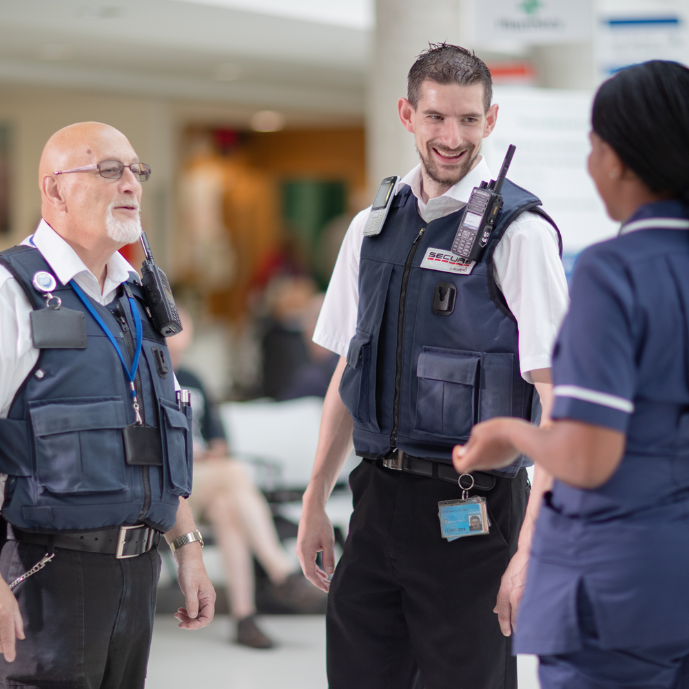 A couple of security personnel talking to a nurse in the hospital