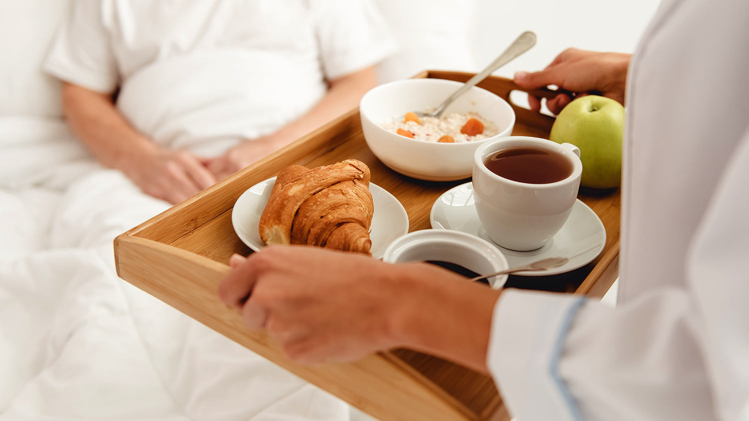 A tray of food being delivered to a patient in a hospital bed