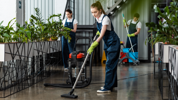 A woman and a man cleaning an office and a woman taking care of the plants