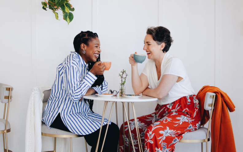 Two women sitting at the table drinking coffee and smiling