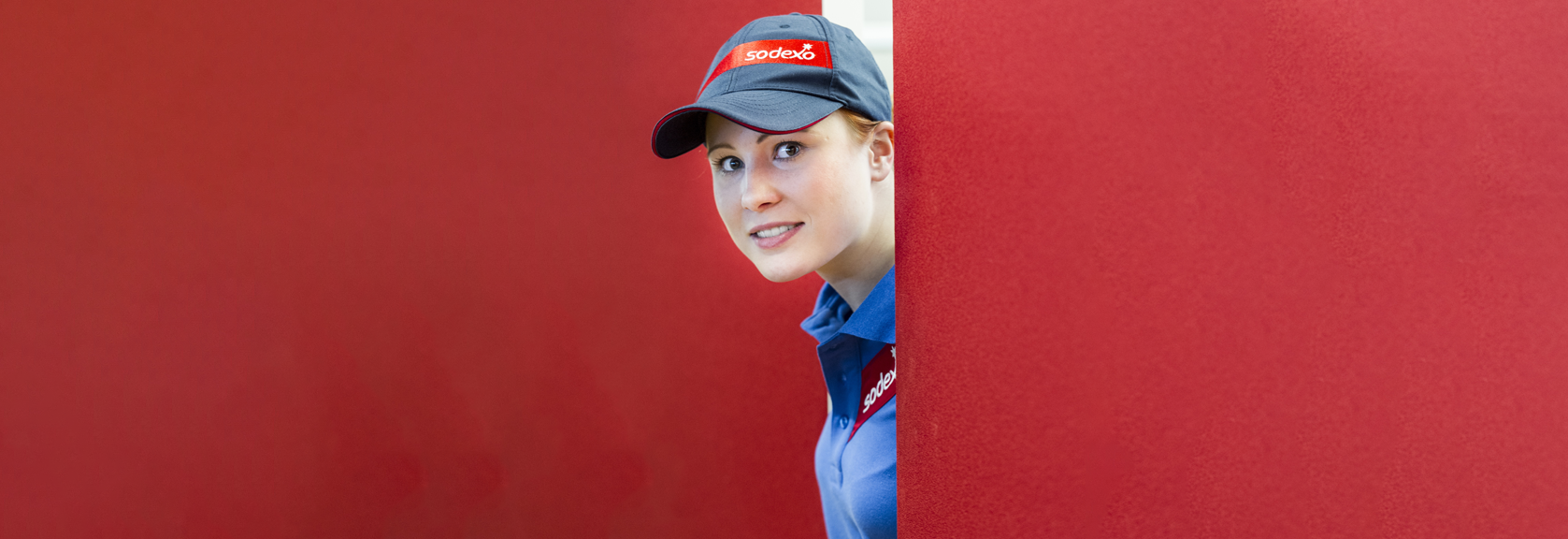 A Sodexo colleague poking her head around a red wall