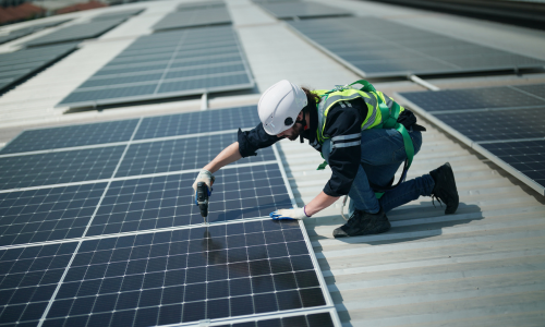 A man in a hard hat and safety vest diligently working on solar panels, ensuring their proper installation and maintenance.