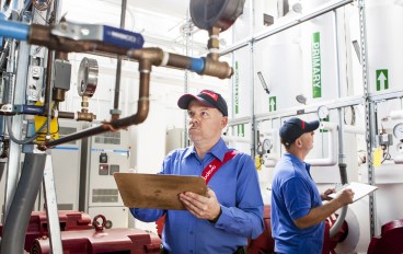 Two men in blue shirts and red hats standing in front of a water heater